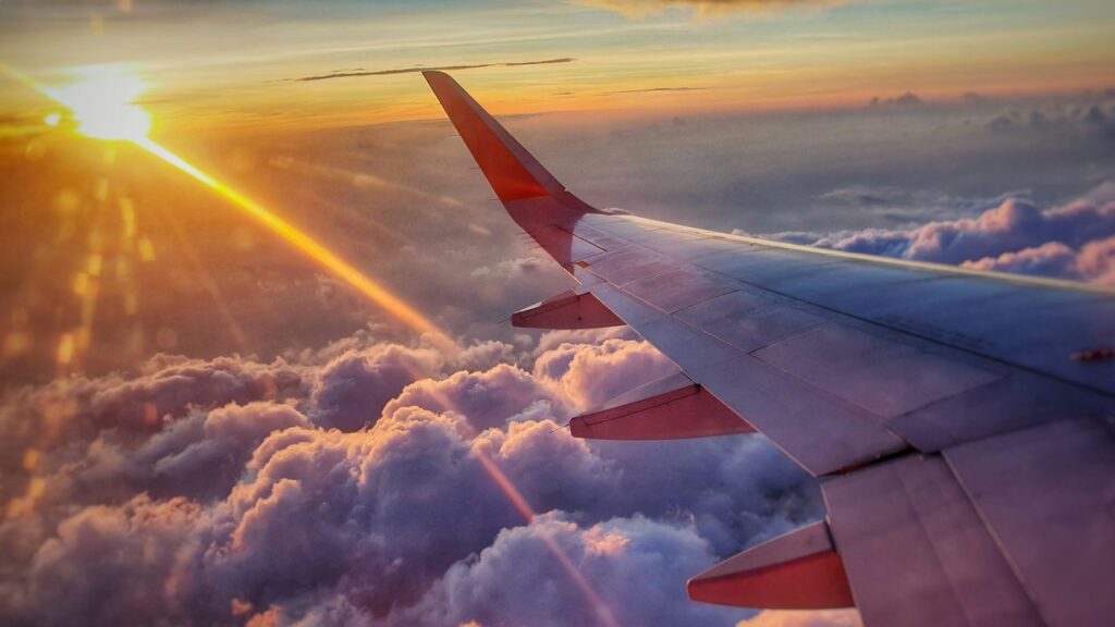 夕焼けの雲の上を飛ぶ旅客機の翼(イメージ)