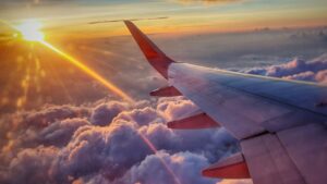 夕焼けの雲の上を飛ぶ旅客機の翼(イメージ)